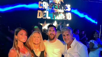 Lionel Messi, Antonela Roccuzzo, Jorge Messi y Celia Cuccittini sonríen en un evento festivo con luces azules y un cartel