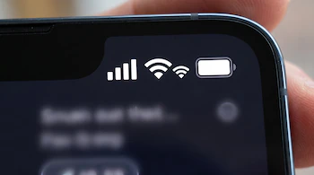 Primer plano de la parte superior de la pantalla de un celular con iconos de señal móvil, WiFi, hotspot, y batería. Un dedo sostiene el dispositivo.